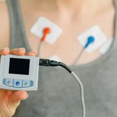Osoba z elektrodami na klatce piersiowej trzyma urządzenie do monitorowania EKG. To urządzenie pomaga zrozumieć, czym jest EKG.