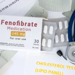 Opakowanie leku Fenofibrate 145 mg, tabletki, stetoskop i wyniki badań cholesterolu.