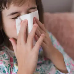 Dziecko z chusteczką przy nosie, być może potrzebuje antybiotyku na zatoki.