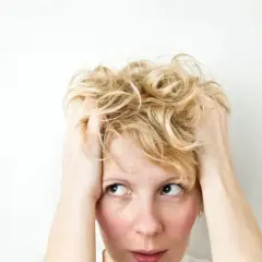 Kobieta z blond włosami, trzymająca się za głowę, z wyrazem niepokoju na twarzy, jakby doświadczała wahań nastroju związanych z cyklotymią.