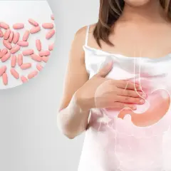 Kobieta z bólem brzucha, obok tabletki. Leki z grupy inhibitory pompy protonowej pomagają złagodzić dolegliwości.