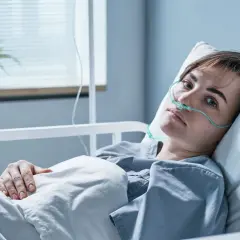 Młoda kobieta w szpitalnym łóżku, z tlenem w nosie, walczy z objawami zapalenia opon mózgowych.