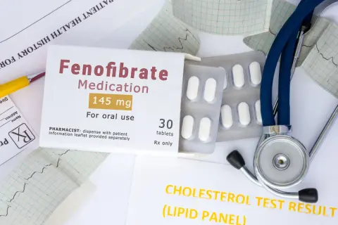 Opakowanie leku Fenofibrate 145 mg, tabletki, stetoskop i wyniki badań cholesterolu.