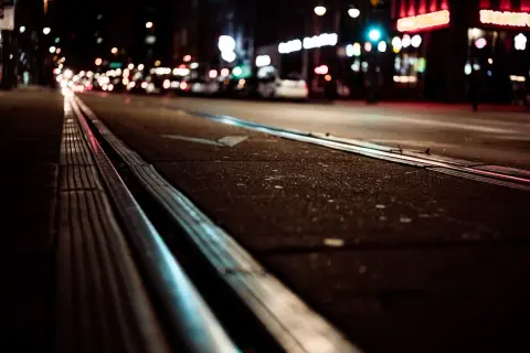 Nocne miasto, tory tramwajowe i światła samochodów tworzą obraz przypominający kurzą ślepotę.