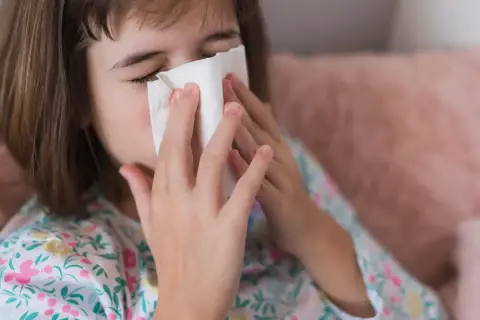 Dziecko z chusteczką przy nosie, być może potrzebuje antybiotyku na zatoki.
