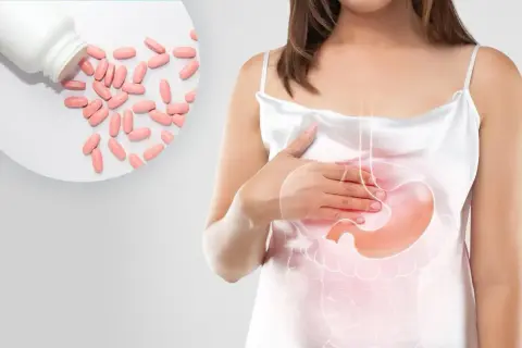 Kobieta z bólem brzucha, obok tabletki. Leki z grupy inhibitory pompy protonowej pomagają złagodzić dolegliwości.
