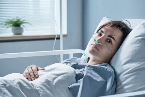 Młoda kobieta w szpitalnym łóżku, z tlenem w nosie, walczy z objawami zapalenia opon mózgowych.