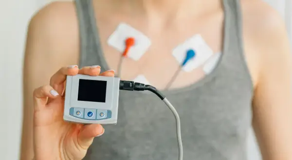 Osoba z elektrodami na klatce piersiowej trzyma urządzenie do monitorowania EKG. To urządzenie pomaga zrozumieć, czym jest EKG.