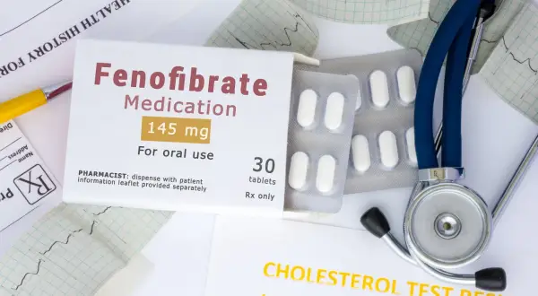 Opakowanie leku Fenofibrate 145 mg, tabletki, stetoskop i wyniki badań cholesterolu.