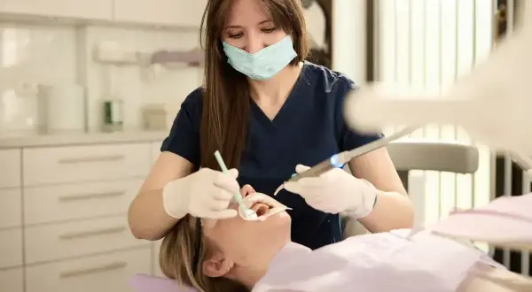 Dentystka w masce i rękawiczkach wykonuje zabieg stomatologiczny u pacjentki.