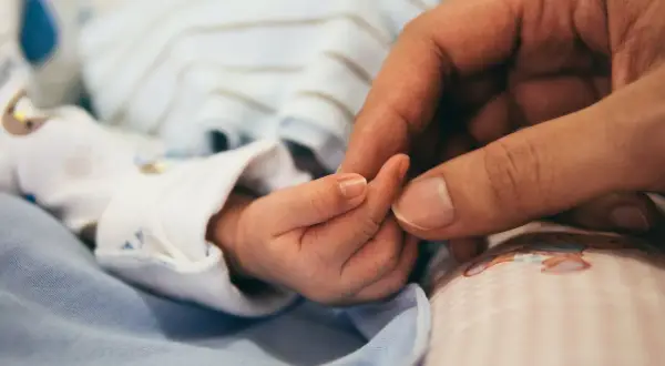 Dłoń dorosłego obejmuje maleńką dłoń dziecka. To obraz miłości i wsparcia, symbol nadziei dla rodzin z zespołem Patau.