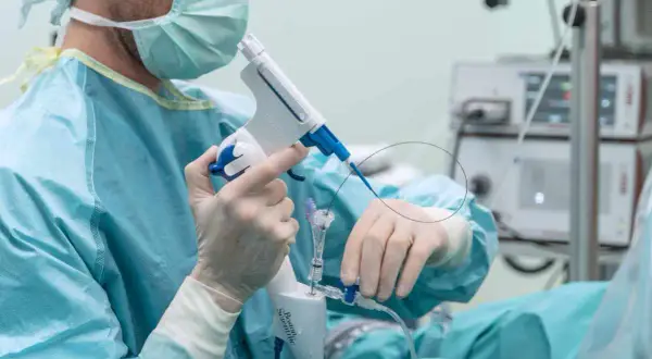 Chirurg w masce i rękawiczkach przygotowuje się do biopsji prostaty, trzymając specjalistyczny przyrząd.