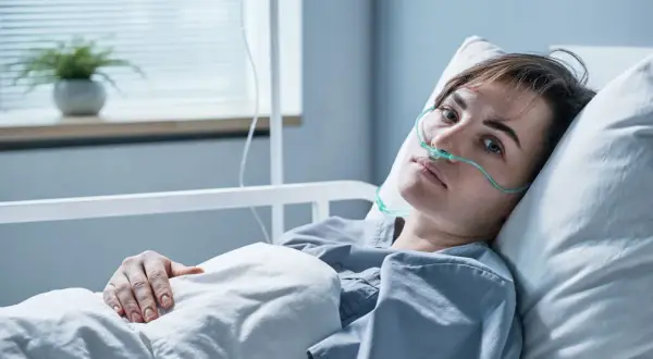 Młoda kobieta w szpitalnym łóżku, z tlenem w nosie, walczy z objawami zapalenia opon mózgowych.