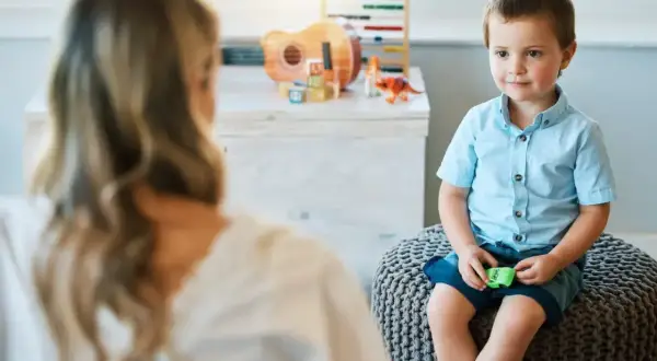 Chłopiec w niebieskiej koszuli siedzi na pufie, rozmawiając z psychologiem.