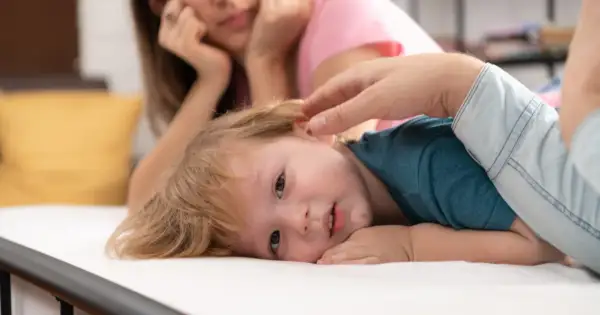 Małe dziecko z blond włosami leży na białym materacu, jego mama patrzy z troską. Czy to początek pandas choroba?