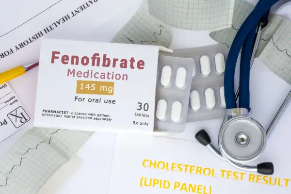 Opakowanie leku Fenofibrate 145 mg, tabletki, stetoskop i wyniki badań cholesterolu.