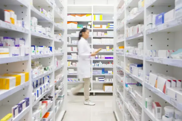 Farmaceutka w białym fartuchu idzie między regałami pełnymi leków, szukając milurit 300.