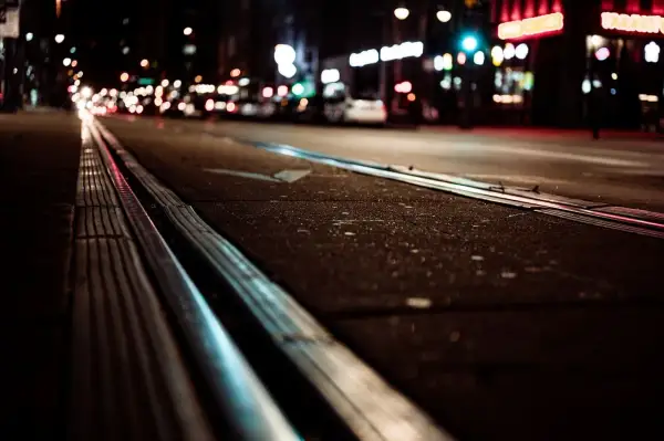 Nocne miasto, tory tramwajowe i światła samochodów tworzą obraz przypominający kurzą ślepotę.