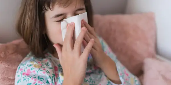Dziecko z chusteczką przy nosie, być może potrzebuje antybiotyku na zatoki.