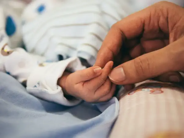 Dłoń dorosłego obejmuje maleńką dłoń dziecka. To obraz miłości i wsparcia, symbol nadziei dla rodzin z zespołem Patau.