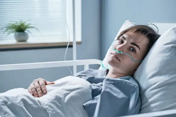 Młoda kobieta w szpitalnym łóżku, z tlenem w nosie, walczy z objawami zapalenia opon mózgowych.
