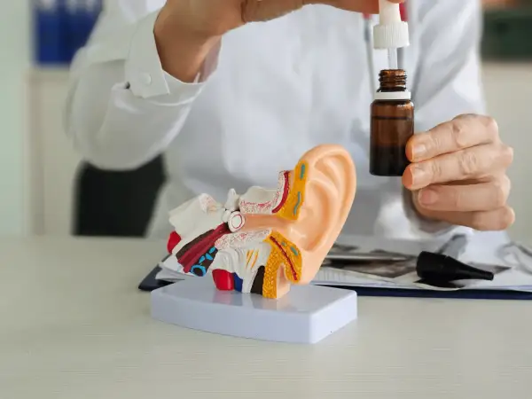 Lekarz pokazuje model ucha i krople, które mogą być antybiotykiem na zapalenie ucha.